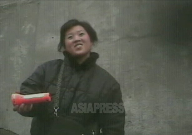 아파트가의 노천 시장에서 여성이 웃는 얼굴로 손전등을 팔고 있다. 2008년 12월 평양시 사동구역에서 촬영 이송희(아시아프레스)